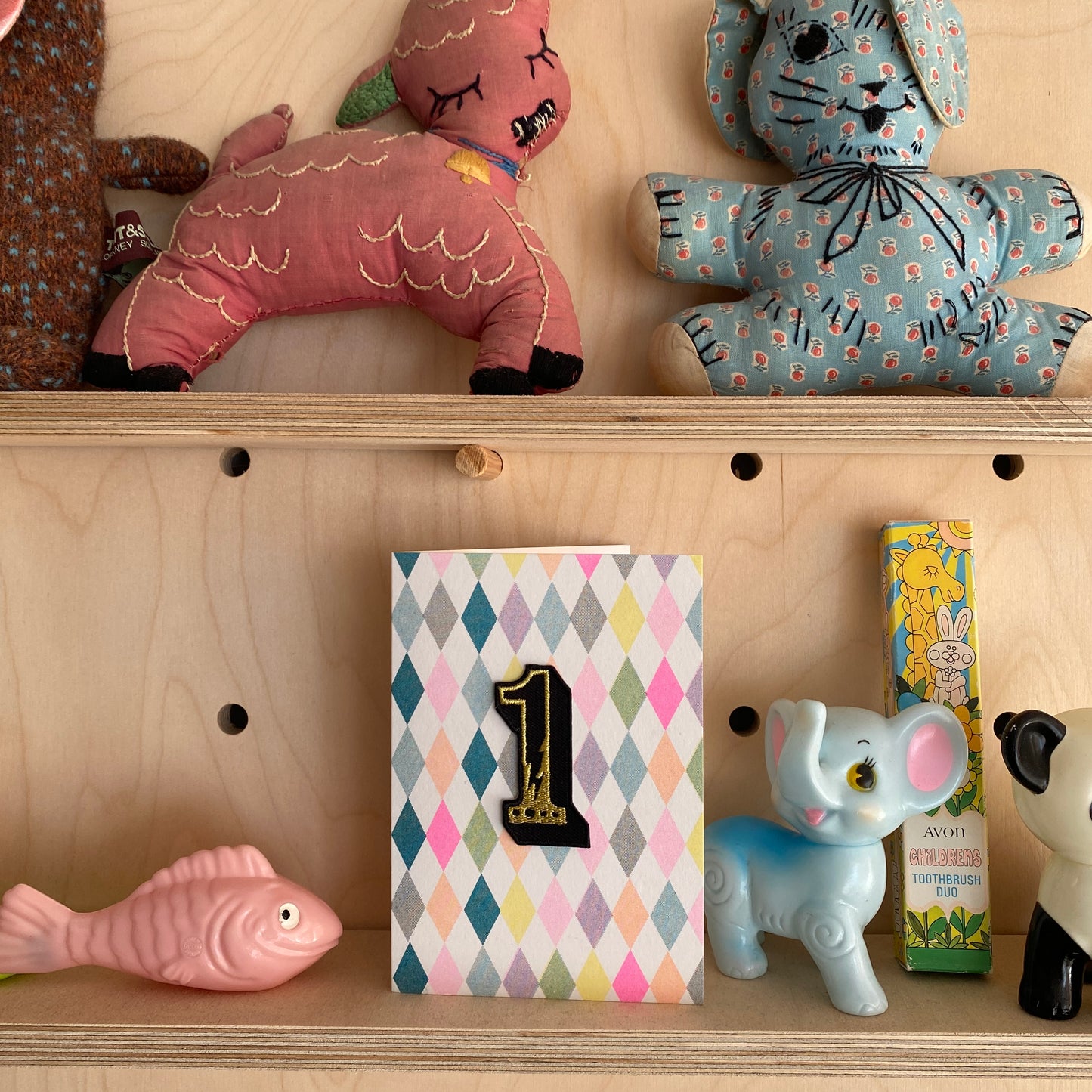 Age 1 birthday harlequin print card on a shelf with vintage toys