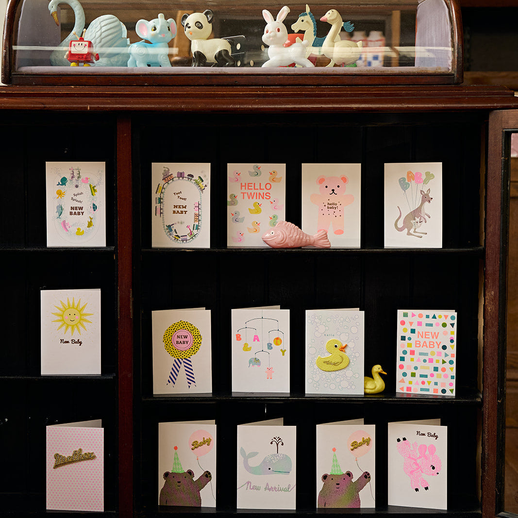 Display case with small figurines and new baby greeting cards on a wooden shelf.