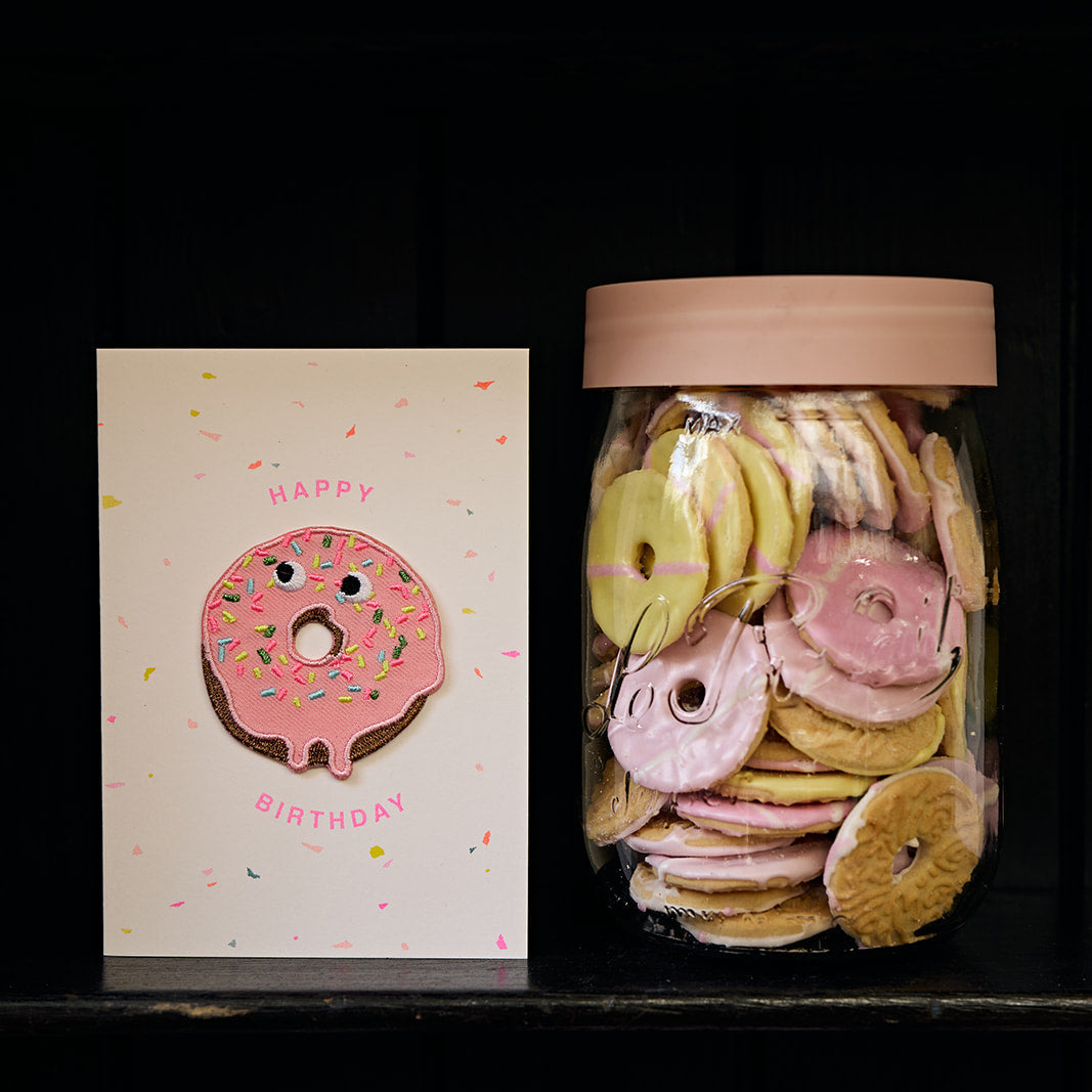 Jar of decorative donut cookies with a 'Happy Birthday' card on a dark surface