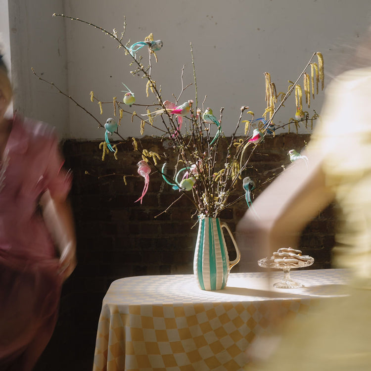 Feather bird clips on branches of flowers in a vintage jug