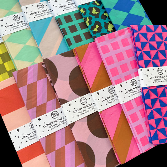 A set of folded luxury tissue paper packs arranged in a fan shape, showcasing various colorful geometric and abstract patterns. The packs are wrapped in white paper bands labeled 'LUXURY TISSUE PAPER' 