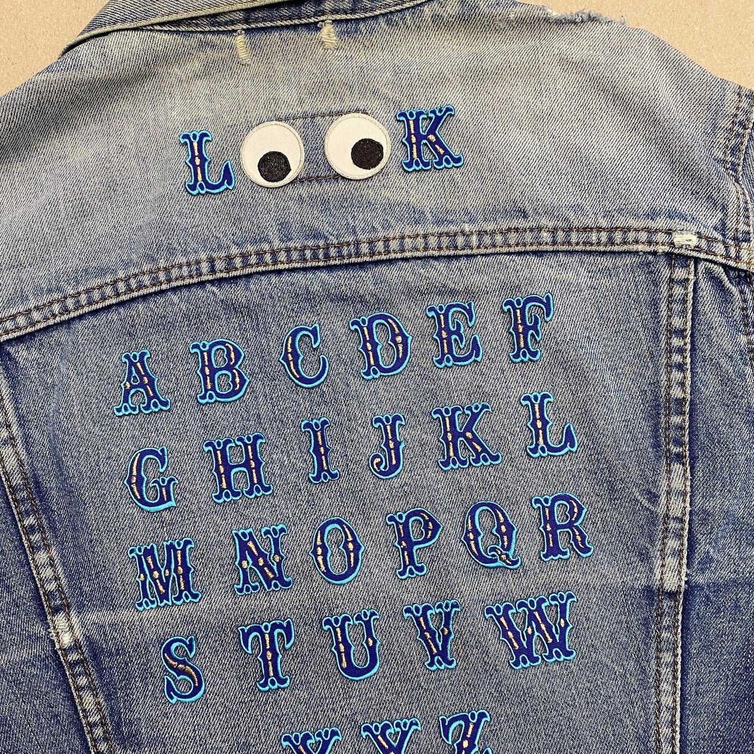 Blue alphabet iron on patches on a denim jacket.