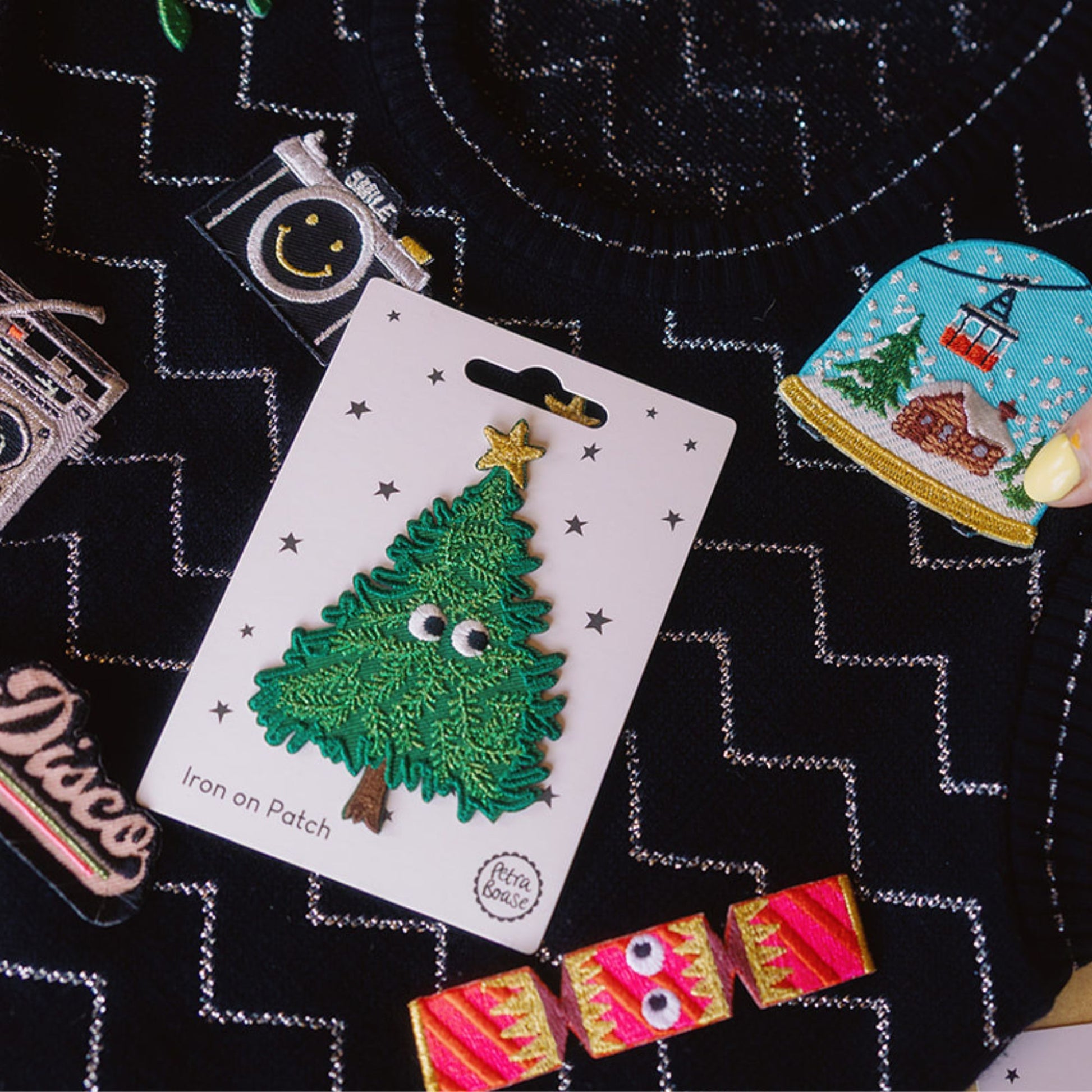 Christmas tree iron-on patch on a white card with other decorative patches on a black sparkly vintage jumper.