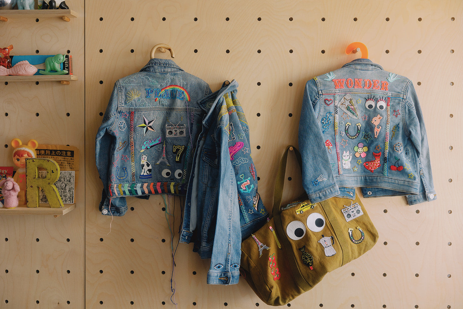 Hand embroidered kids denim jackets and bag hangingon pegboard.