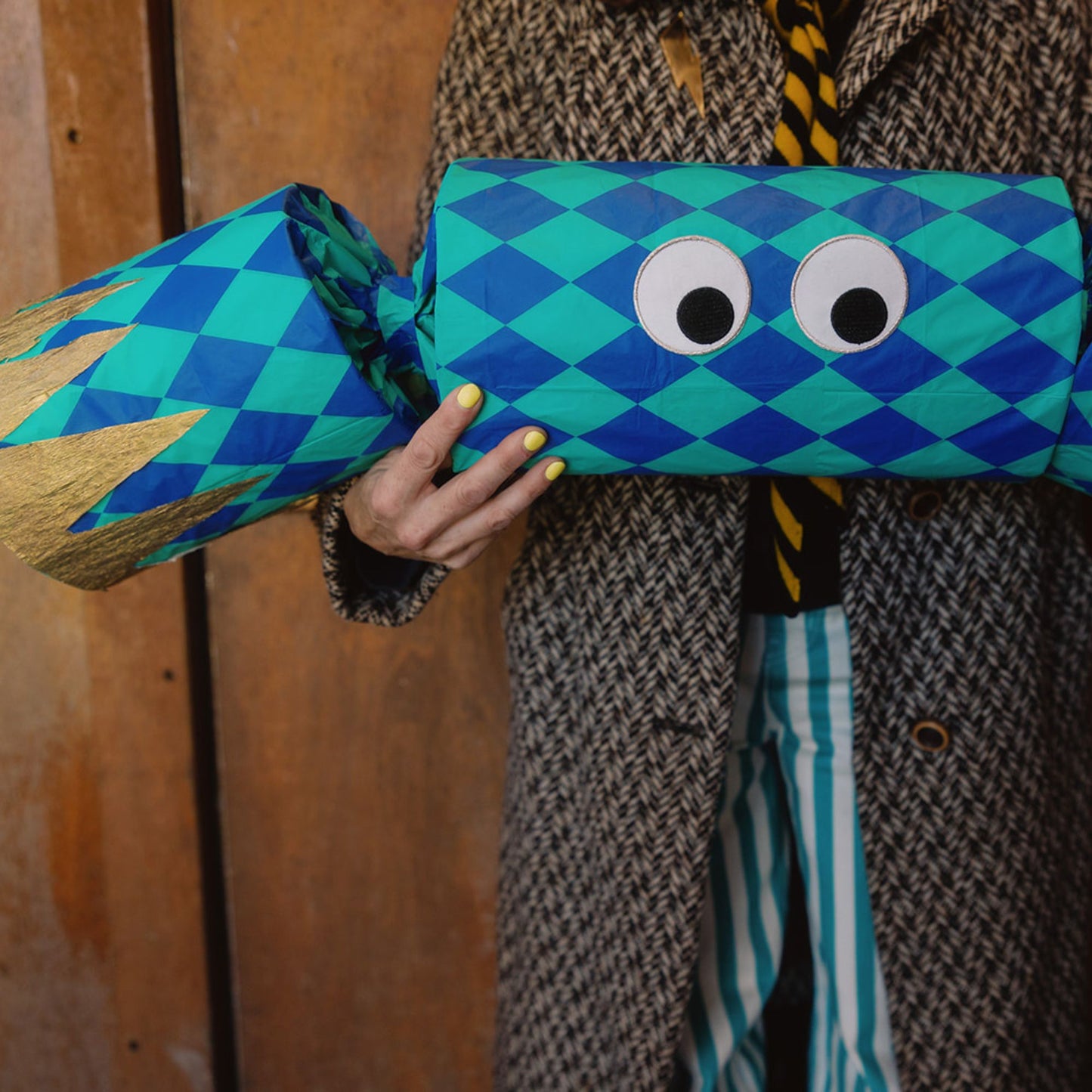 Person holding a blue diamond print cracker with googly eyes against a wooden background.