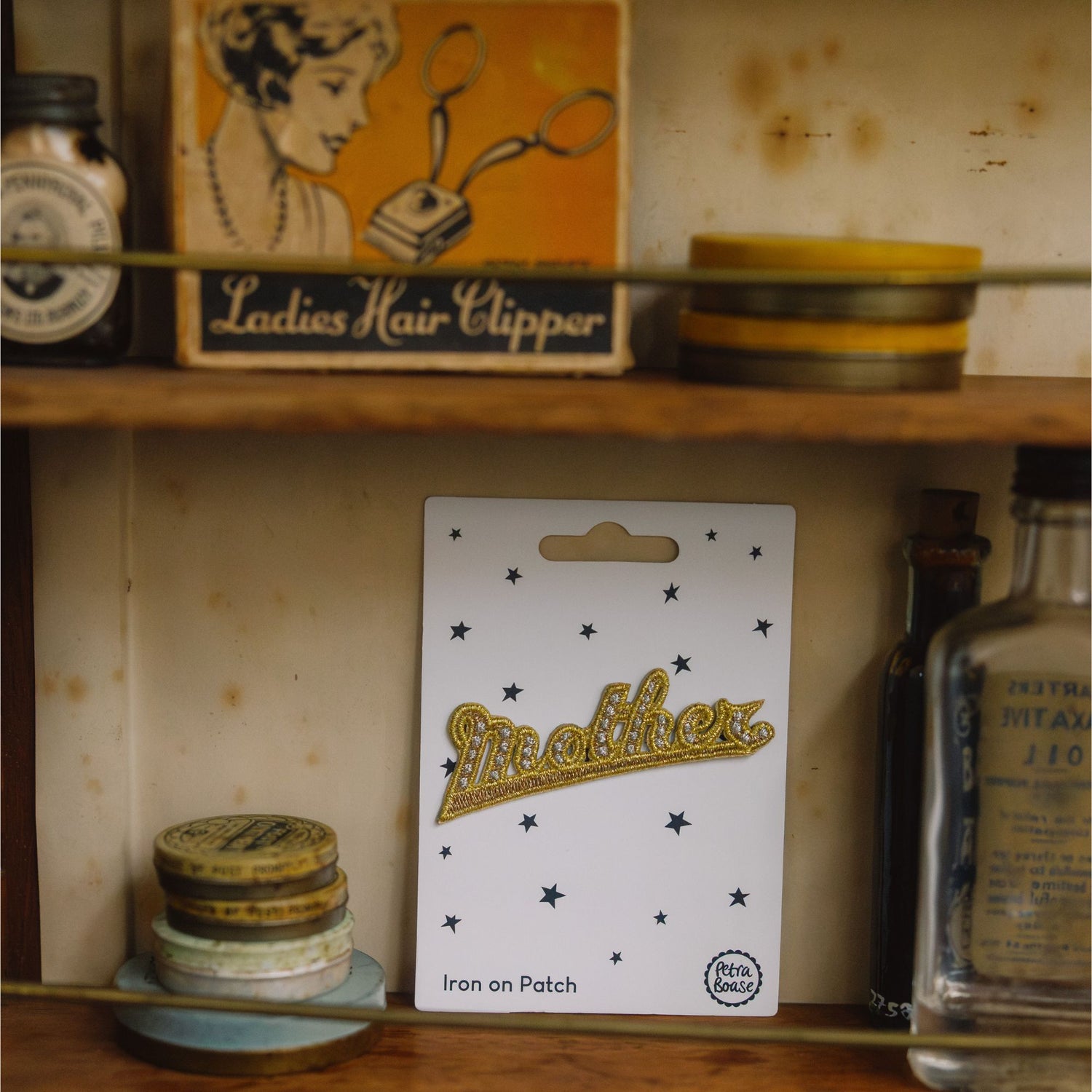 Shelf with vintage items including a 'Ladies Hair Clipper' box and a 'Mother' brand iron-on patch.
