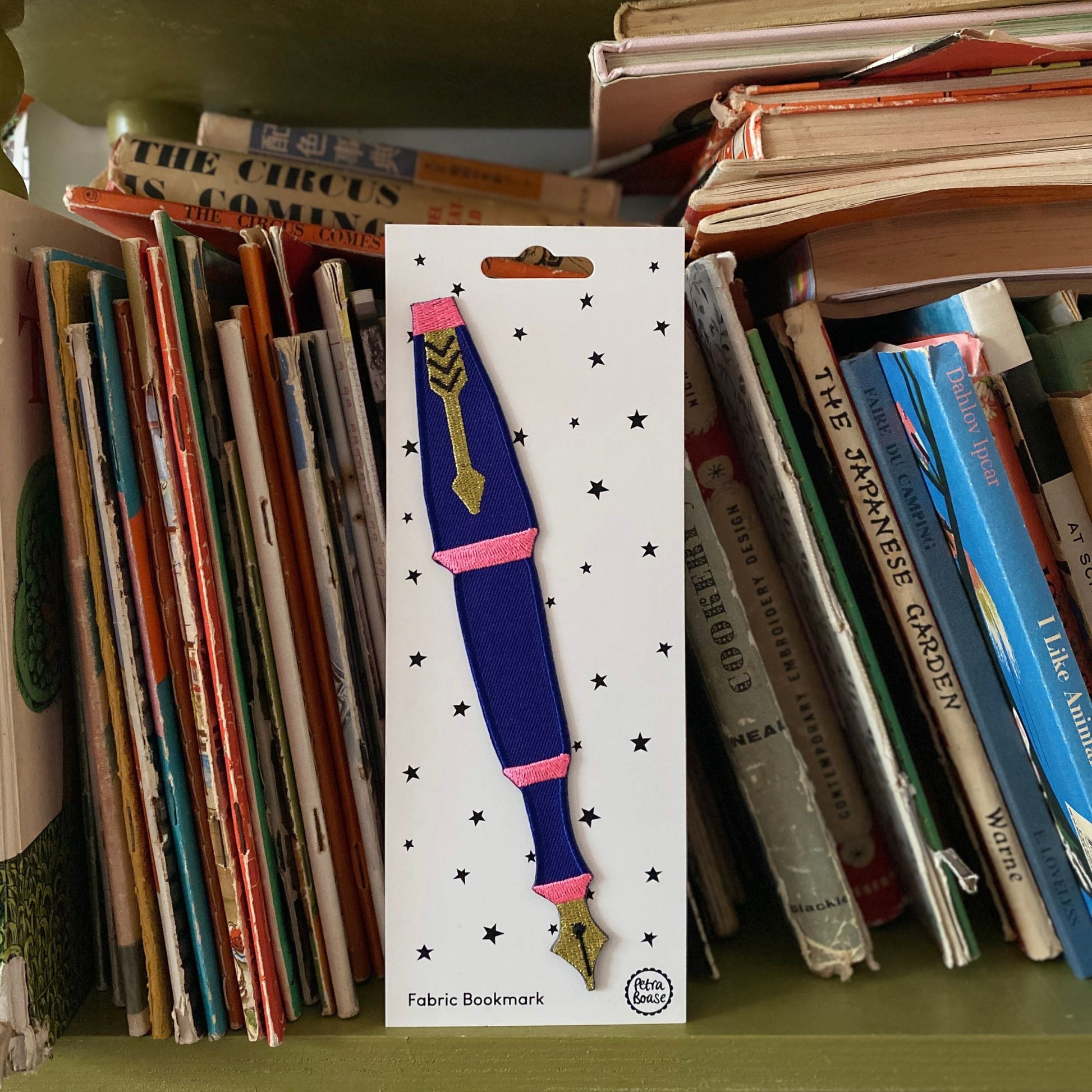 Fabric bookmark with decorative design on a card, surrounded by books