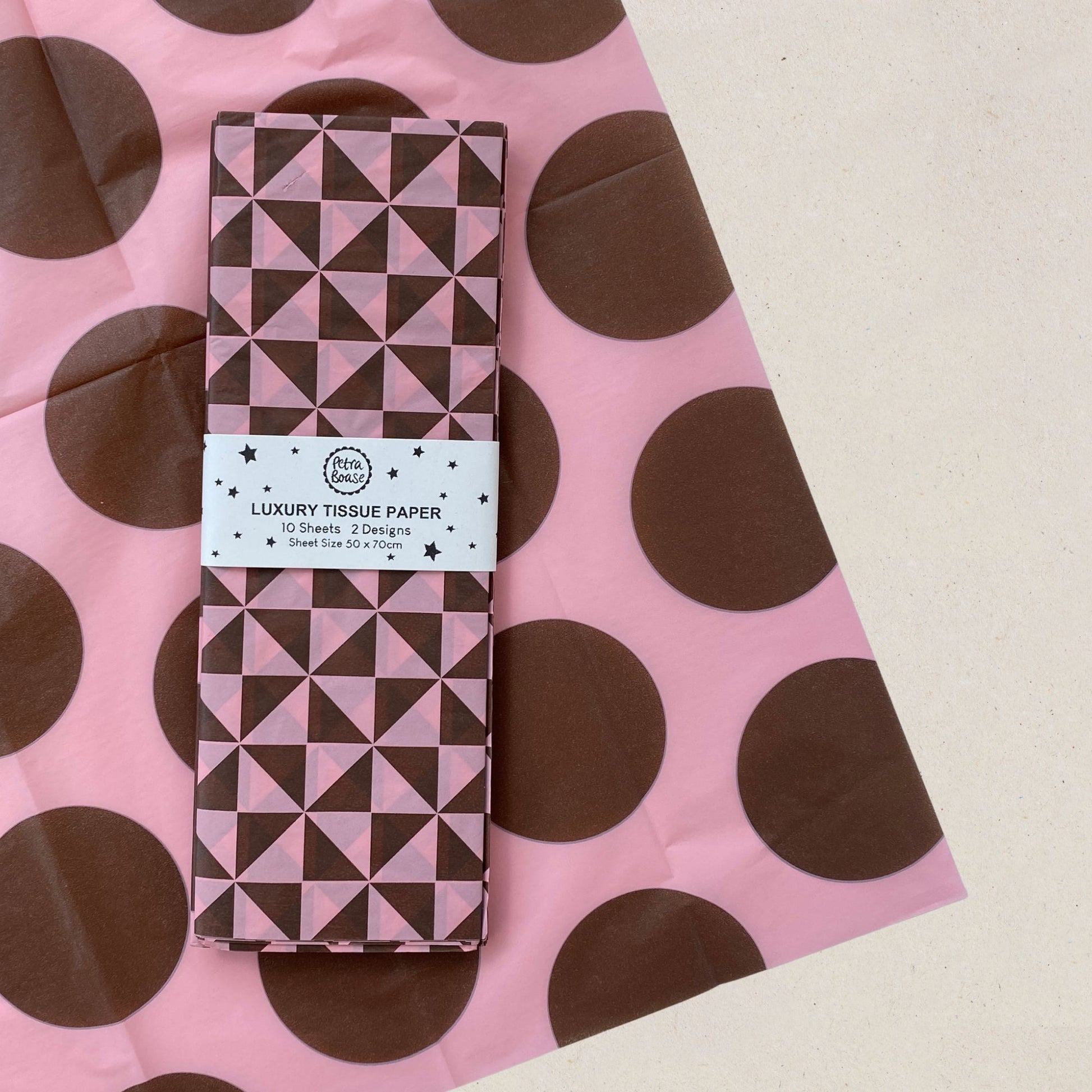 A roll of patterned luxury tissue paper wrapped in a white paper band labeled 'LUXURY TISSUE PAPER  placed on top of a pink tissue paper sheet with large brown polka dots.