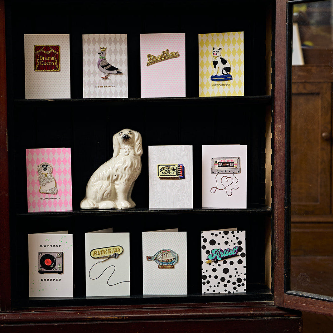 Collection of greeting cards displayed on a wooden shelf with a decorative dog figurine.