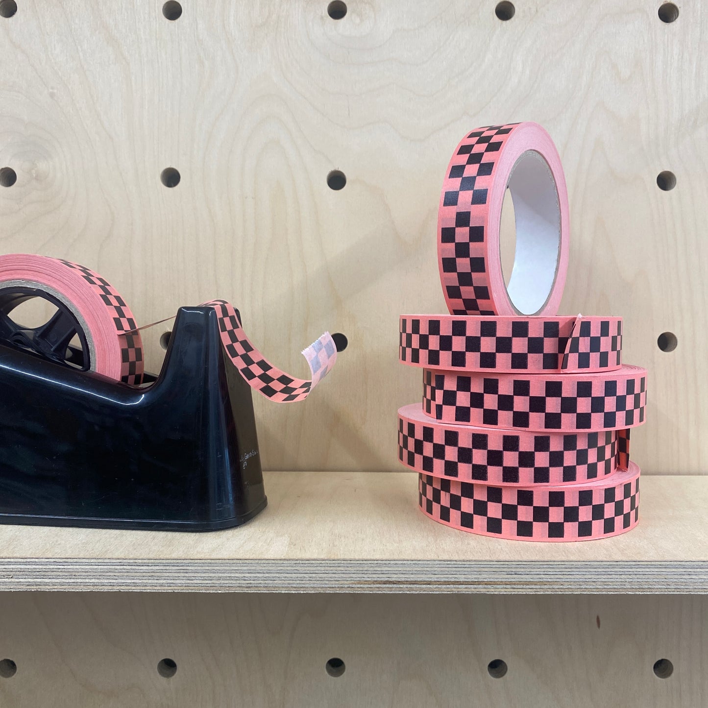 Rose pink Eco paper adhesive tape with black chequerboard  print on a shelf.