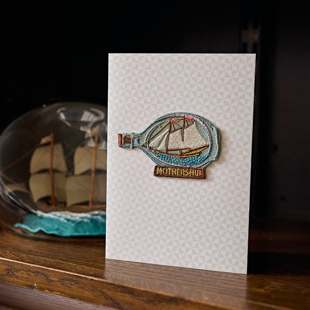 Card with a ship in a bottle design on a wooden surface
