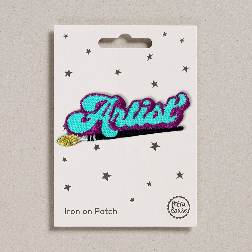 A packaged 'Artist' iron on patch with blue, purple, black, and gold embroidered detailing, displayed on a card with stars.