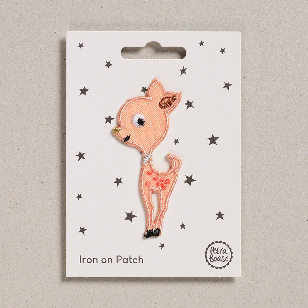 A packaged iron on patch depicting a cute baby deer in peach color with multi-colored embroidery, displayed on a card with stars.