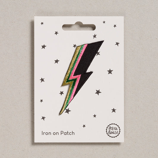 A packaged 'Petra Boase | Lightening Bolt Iron on Patch' with an iron-on backing, featuring a black bolt with multicolored embroidered detailing, displayed on a card with stars.
