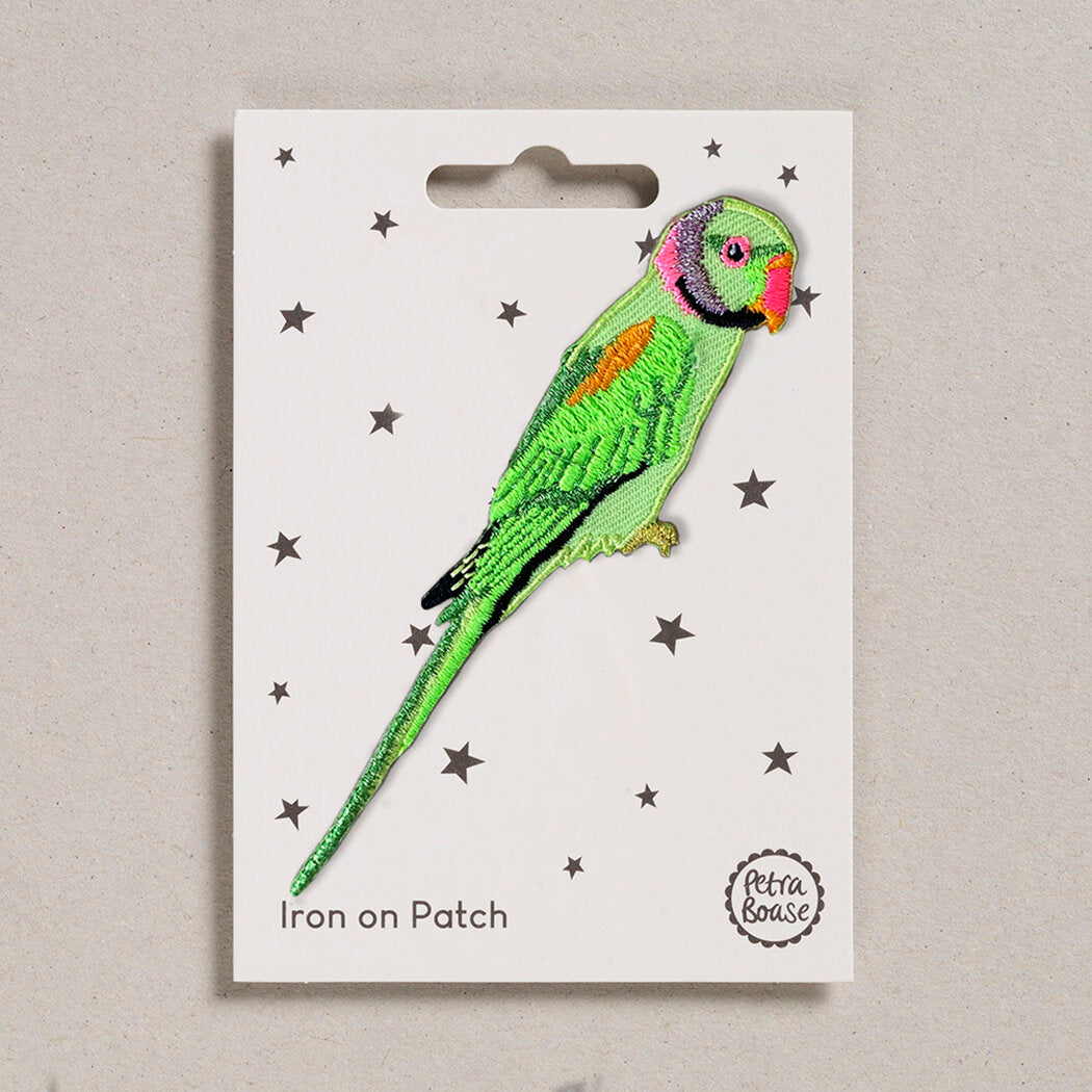 A packaged 'Petra Boase Parrot Iron on Patch' featuring an embroidered green parrot with multicolored details on a white background with stars.